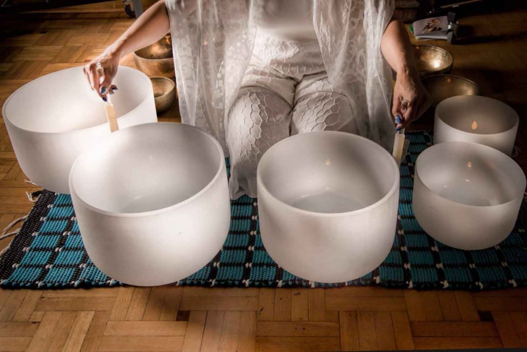 Person sitting with singing bowls arranged on a blue mat, used for sound healing and meditation therapy
